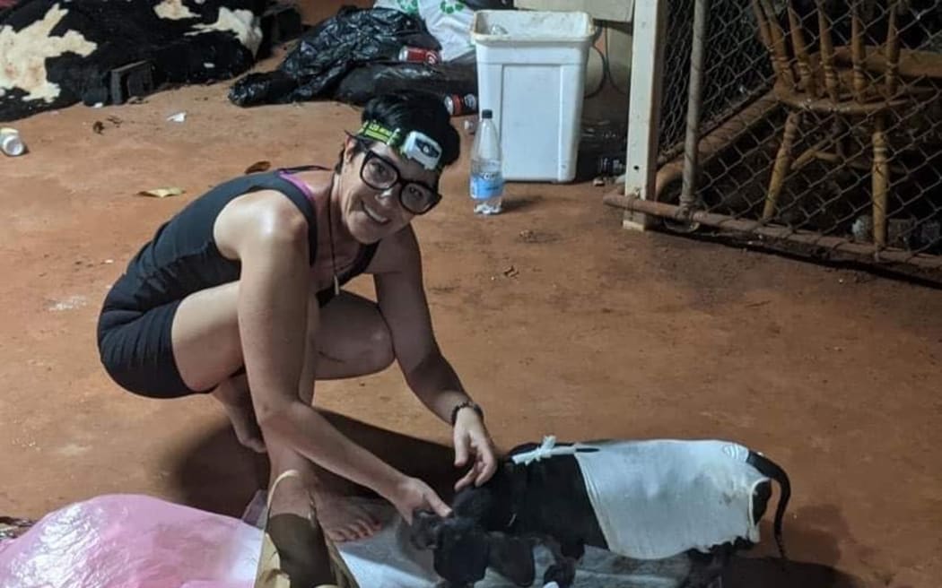 Kiwi nurse Sandra McMullan is crouching on a floor. She is wearing a head torch. There is a small black dog at her feet,