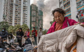 Residents check clothing donated for them after a major fire swept through several apartment blocks at the Wang Fuk Court residential estate in Hong Kong's Tai Po district on November 27, 2025. Hong Kong firefighters were scouring a still-burning apartment complex for hundreds of missing people on November 27, a day after the blaze tore through the high-rises, killing at least 44. (Photo by Dale DE LA REY / AFP)