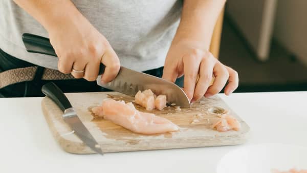 A person chopping chicken on a board in a kitchen.