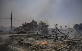 This photograph taken on July 24, 2023, shows firefighting vehicles parked outside houses amid a fire between the villages of Kiotari and Genadi, on the Greek island of Rhodes. Firefighters tackled blazes that erupted in peak tourism season, sparking the country's largest-ever wildfire evacuation -- and leaving flights and holidays cancelled. Tens of thousands of people have already fled blazes on the island of Rhodes, with many frightened tourists scrambling to get home on evacuation flights. (Photo by Spyros BAKALIS / AFP)