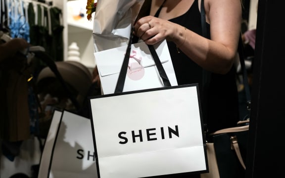 (FILES) A customer holds her bags as she leaves a pop-up store of the Chinese-founded fast fashion brand Shein, in Dijon on June 26, 2025. Italy's competition watchdog said on August 4, 2025, it has fined the company responsible for Shein's websites in Europe one million euros ($1.15 million) for false and confusing claims about the e-commerce giant's efforts to be environmentally "green". (Photo by ARNAUD FINISTRE / AFP)
