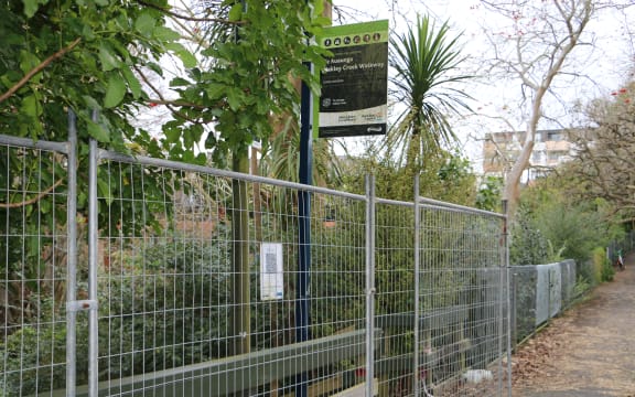 A sign for the Oakley Creek walkway, with a fence in front of it.