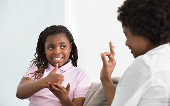 Smiling Young Mother Learning Sign Language To Talk With Her Hearing Impairment Daughter