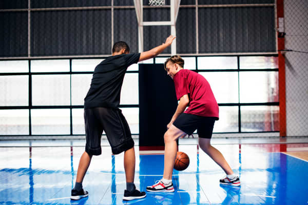 Two boys play basketball indoors.