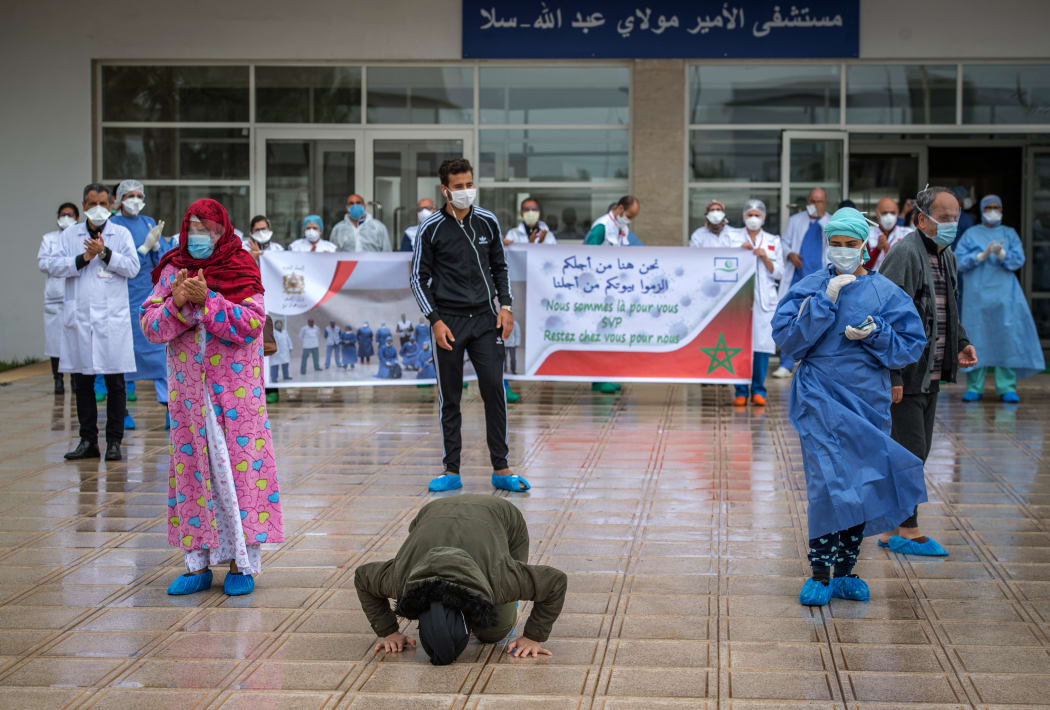 A patient who recovered from Covid-19 disease kisses the ground as another rejoices as they leave a hospital in Morocco, 12 April.