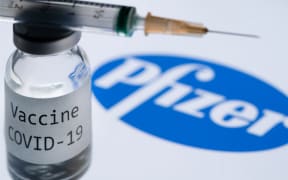 File: This illustration picture taken in Paris on November 23, 2020 shows a syringe and a bottle reading "Covid-19 Vaccine" next to the Pfizer company logo.