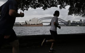 People run before the Opera House and Harbour Bridge in Sydney on December 20, 2020, after authorities introduced a fresh round of restrictions.