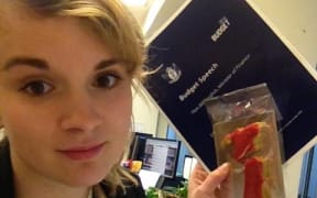 Elle holding the budget documents and a sugar cookie shaped like New Zealand