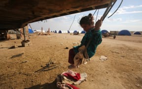 A displaced Iraqi girl plays on a swing at the Al-Agha camp where Iraqi families from the nearby villages of Tal Afar, southwest of Mosul, are taking shelter as Iraqi forces continue their military operation to recapture Mosul from Islamic State (IS) jihadists on February 16, 2017.