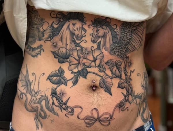 A person lifting their shirt, showing tattoo of horses and flowers covering their torso.