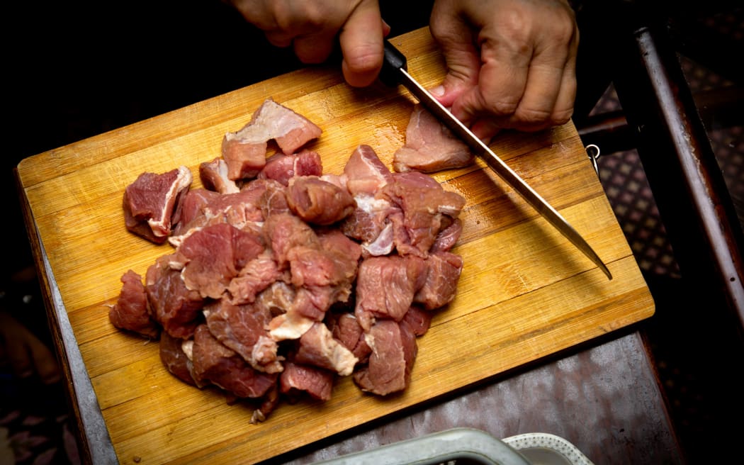 A person chops raw meat on a wooden chopping board.