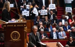 Members of Parliament of left-wing coalition NUPES (New People's Ecologic and Social Union) hold placards as France's Prime Minister Elisabeth Borne (C) arrives to confirm to force through pension law without parliament vote during a session on the government's pension reform at the lower house National Assembly, in Paris on March 16, 2023. - French President forced through pension law without parliament vote, after he  won approval from the upper house Senate for his reform of the pension system, which has sparked massive protests and strikes since the start of the year.