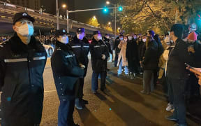 Police officers watch protesters gathering along a Beijing street during a rally for the victims of a deadly fire and a protest against China's harsh Covid-19 restrictions, 28 November, 2022.
