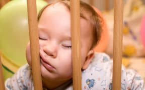 Baby sleeps with funny face in the playpen