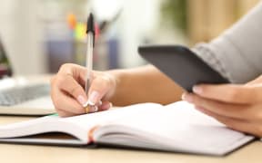 Woman writing and consulting a mobile phone on a desk at home or office