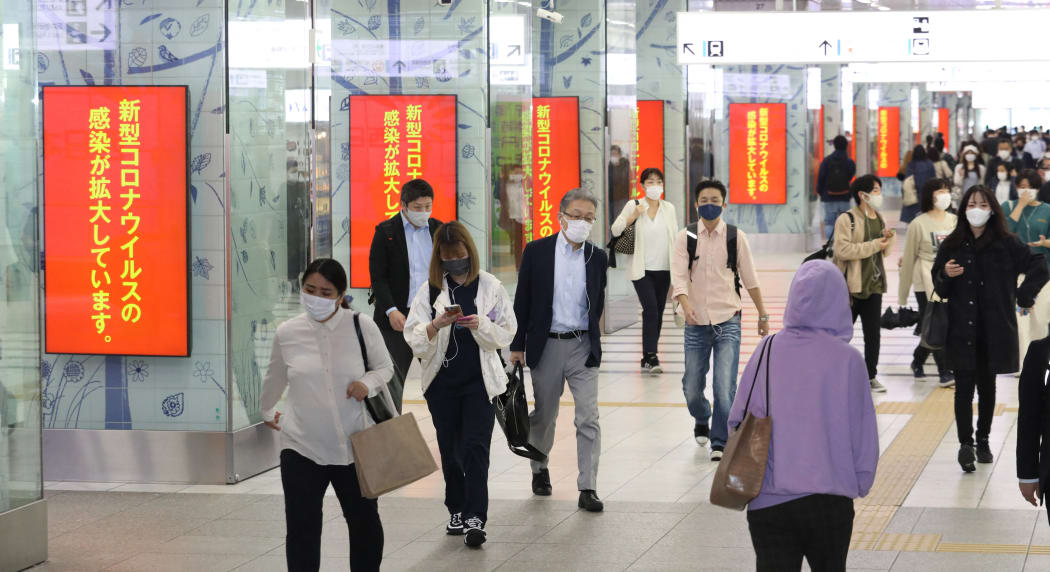 Commuters in Fukuoka City pass electronic billboards calling for the prevention of the spread of Covid-19.