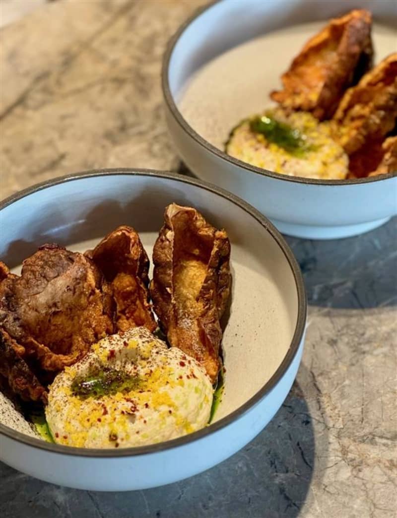 A bowl of tarama dip garnished with fried Jerusalem artichoke skins.