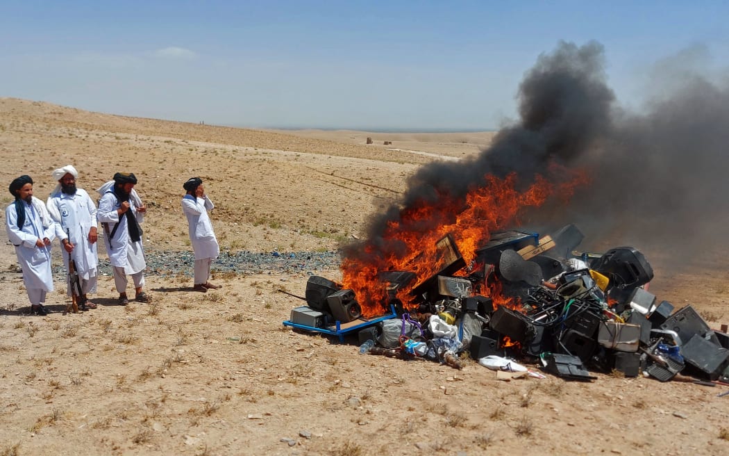 In this handout photograph taken on July 29, 2023 and released by the Afghanistan's Ministry for the Propagation of Virtue and the Prevention of Vice, members of Taliban stand guard after setting fire to a pile of musical instruments and equipments on the outskirts of Herat. Authorities from Afghanistan's vice ministry created a bonfire of confiscated musicial instruments and equipment in Herat province at the weekend, deeming music immoral. (Photo by Afghanistan's Ministry for the Propagation of Virtue and the Prevention of Vice / AFP) / RESTRICTED TO EDITORIAL USE - MANDATORY CREDIT "AFP PHOTO/Afghanistan's Ministry for the Propagation of Virtue and the Prevention of Vice" - NO MARKETING NO ADVERTISING CAMPAIGNS - DISTRIBUTED AS A SERVICE TO CLIENTS
