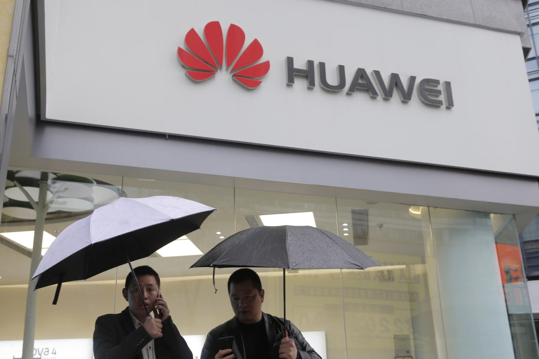 FILE - In this Thursday, March 7, 2019 file photo, two men use their mobile phones outside a Huawei retail shop in Shenzhen, China's Guangdong province.