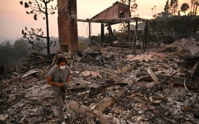 A man carries a bronze statue found amid the rubble of his parents' home, destroyed during the Palisades Fire, in Pacific Palisades, a neighborhood of Los Angeles, California, on January 9, 2025. The two largest fires burning in Los Angeles remain "zero percent" contained on January 9 despite firefighting operations, officials said, as they also vowed to tackle looting of evacuated homes. A 17,000-acre (6,900-hectare) blaze in Pacific Palisades has become "one of the most destructive natural disasters in the history of Los Angeles," said city fire chief Kristin Crowley, while a 10,000-acre fire in Altadena was also at "zero percent containment," said county fire chief Anthony Marrone. (Photo by Patrick T. Fallon / AFP)