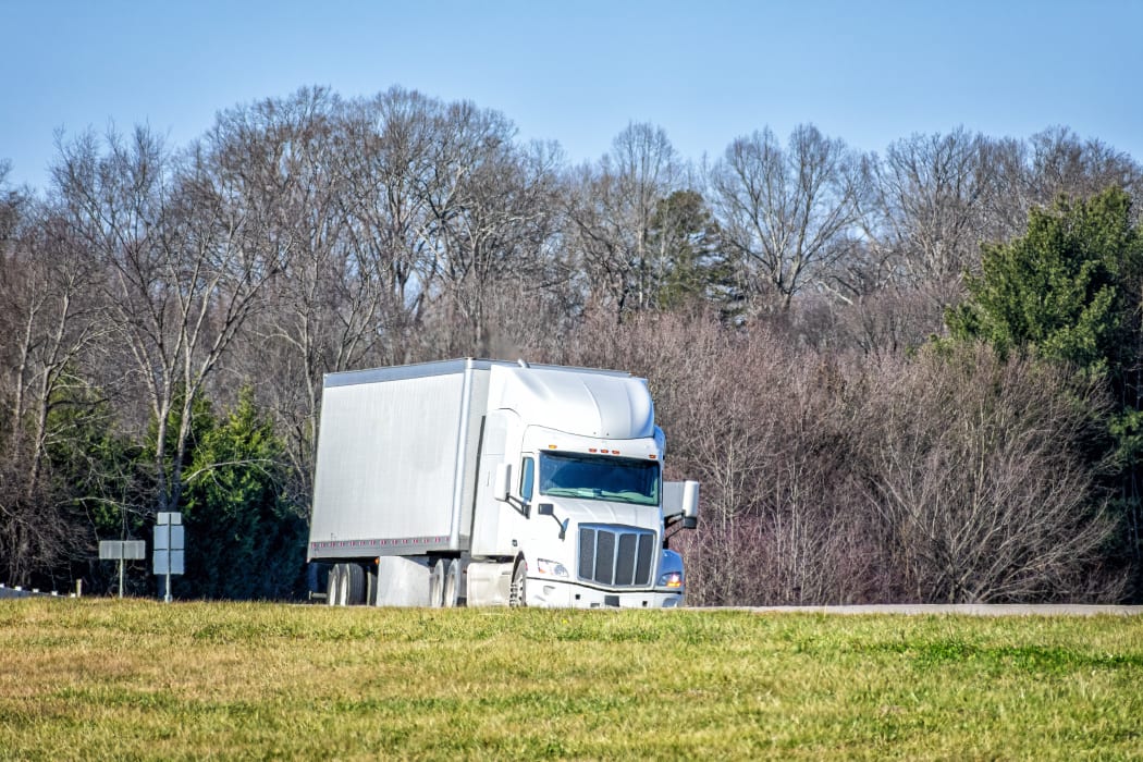 Horizontal shot of a generic white tractor trailer truck on a highway.