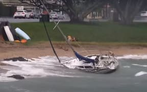 A screenshot from the Hauraki Gulf Weather live camera shows a small boat tipped on its side close to the shoreline.