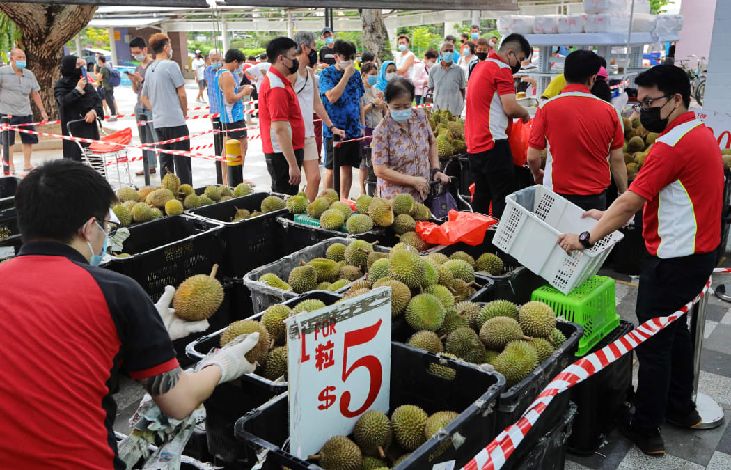 People wait in queue to buy durian on June 24, 2021 in Singapore. On June 21, Singapore entered into a calibrated easing of social management measures as local community COVID-19 cases remain under control.