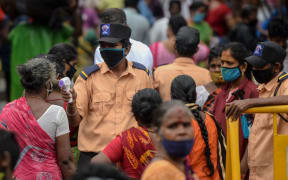 A security personnel (C) checks the body temperature of a woman (C-L) as she enters a market as a preventive measure against the spread of the COVID-19 coronavirus in Chennai on July 29, 2020.
