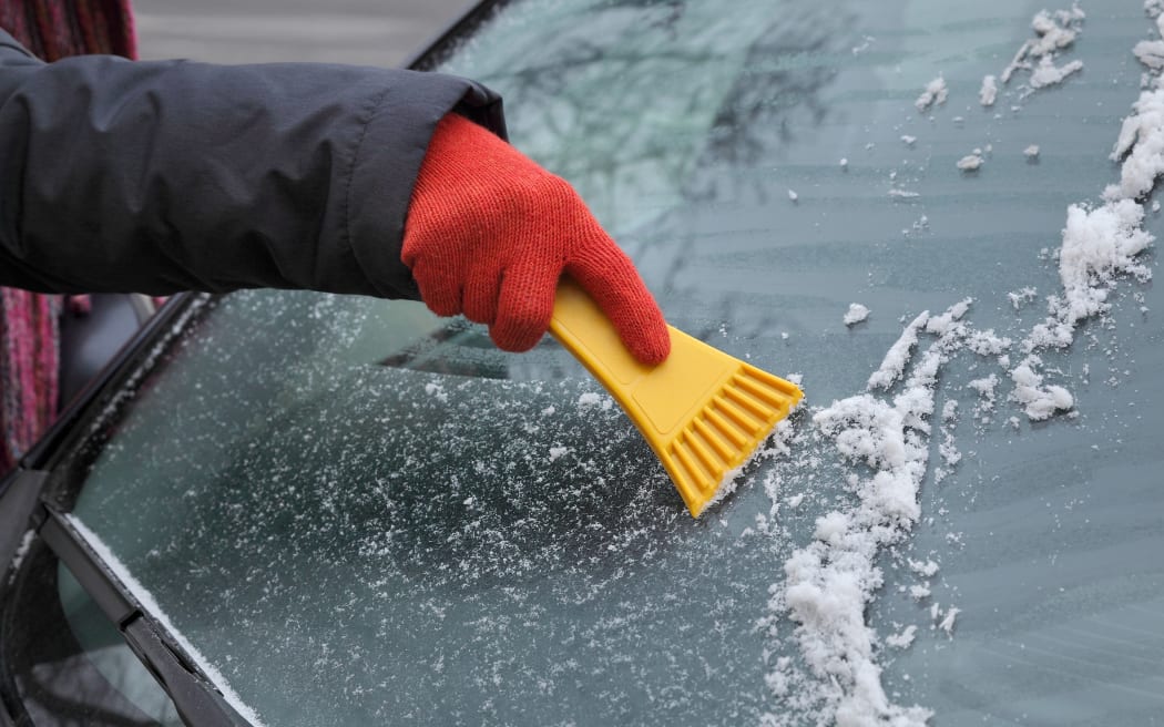 Winter scene, human hand in glove scraping ice from windshield of car