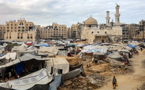 A man carries a jerrycan as he walks past tents sheltering people displaced by war pitched near the heavily-damaged Sheikh Hamad bin Khalifa Al-Thani mosque at the Qatari-built Hamad City residential complex in northwestern Khan Yunis, in the southern Gaza Strip, on 6 October, 2025.