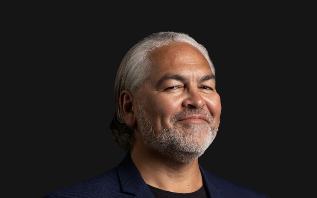 Victor smiles at the camera. He is wearing a navy blazer over a black top.