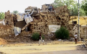 A Sudanese boy looks on as a woman walks past a damaged building in Khartoum's twin-city Omdurman on March 20, 2025. Since April 2023, the conflict has pitted army chief Abdel Fattah al-Burhan against his former deputy and RSF commander Mohamed Hamdan Daglo, leaving thousands dead and uprooting more than 12 million, according to UN figures, with many living in makeshift camps and over 3.5 million fleeing across the country's borders. (Photo by Ebrahim Hamid / AFP)