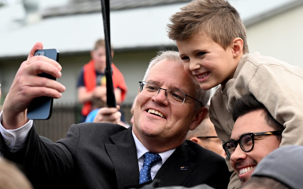 Australian Prime Minister Scott Morrison (L) takes a selfie with a local family after casting his vote outside a polling station during the Australian general election in Sydney on May 21, 2022. (Photo by SAEED KHAN / AFP)