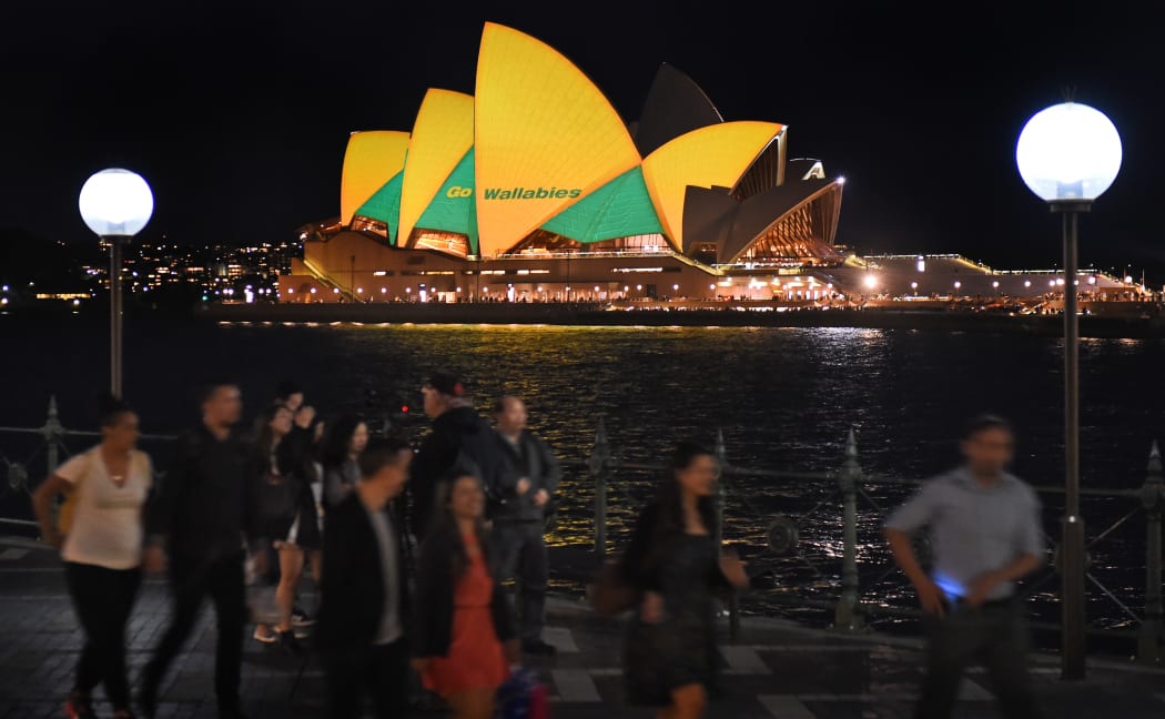 People pass the Sydney Opera House lit up in Australian colours in support of the Wallabies.
