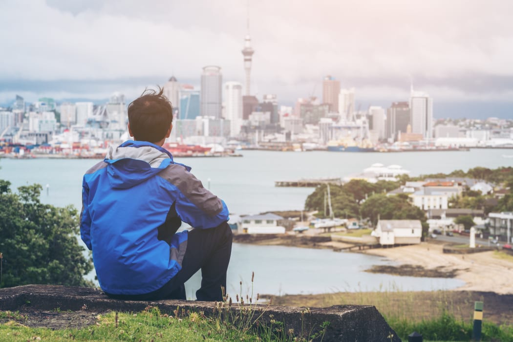 Young man at looking Auckland city skyline of city center and Auckland Sky Tower in New Zealand.
