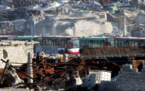 Buses drive through the Syrian government-controlled crossing of Ramoussa, on the southern outskirts of Aleppo, on December 18, 2016, during an evacuation operation of rebel fighters and civilians from rebel-held areas.