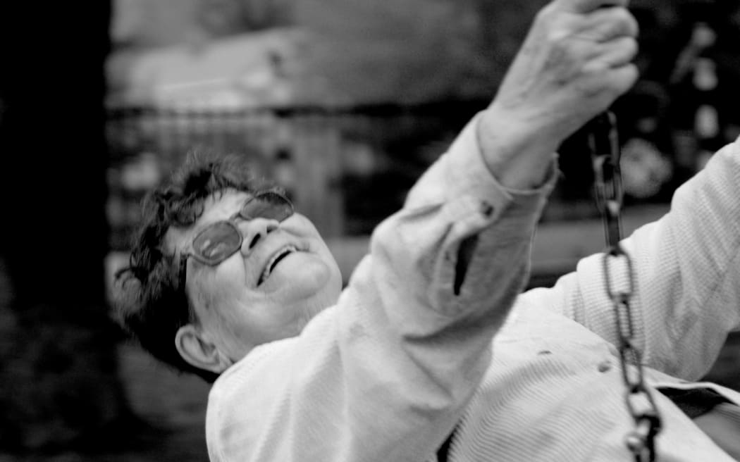 A black-and-white image of a smiling Joy Cowley sitting on a swing.