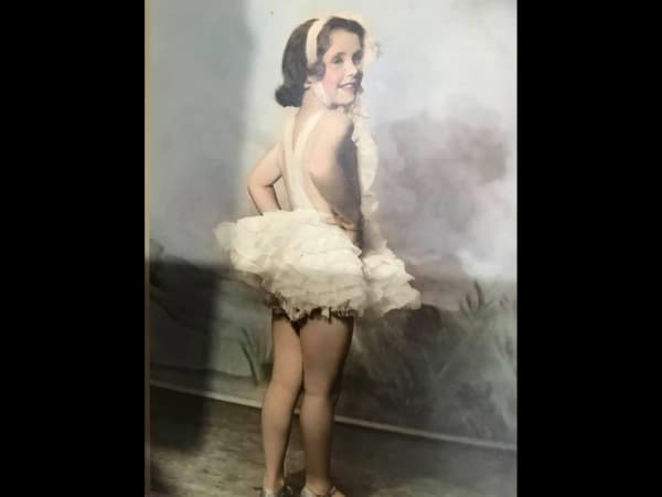 A dark-haired child smiles in a tutu.