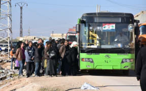 Syrian residents fleeing the violence, queue as they board a bus at a checkpoint, manned by pro-government forces, in the village of Aziza on the southwestern outskirts of the northern Syrian city of Aleppo