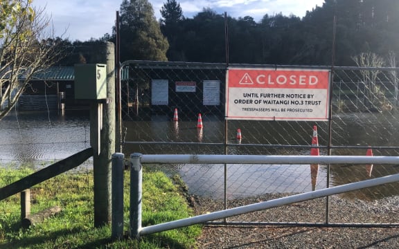 A gate with a large 'closed until further notice' sign. Behind the gate, there is flooding form the nearby lake.