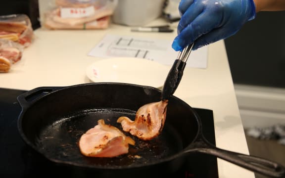 Juges sizzle bacon in a pan.