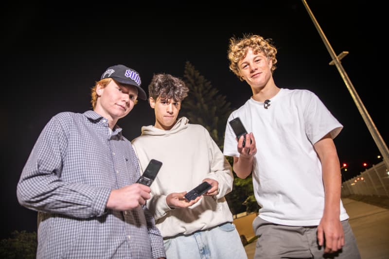 Teens Connor Cummins, Israel Cameron and Isaac Reid hold their brick phones.