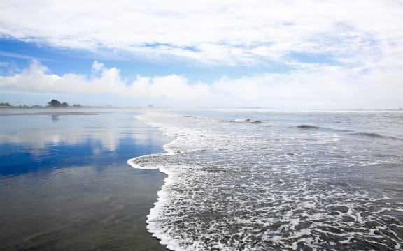 Coastline view on sky background in Westport of New Zealand. Soft waves splashing on sandy beach.
