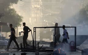 Palestinians walk past burned waste during an Israeli military operation in the Jenin refugee camp in the occupied West Bank on July 3, 2023. Israel has stepped up operations in the northern West Bank, home to Jenin city and its adjacent refugee camp, a stronghold of Palestinian armed groups where there has been a spate of attacks on Israelis as well as attacks by Jewish settlers on Palestinian communities. (Photo by Jaafar ASHTIYEH / AFP)