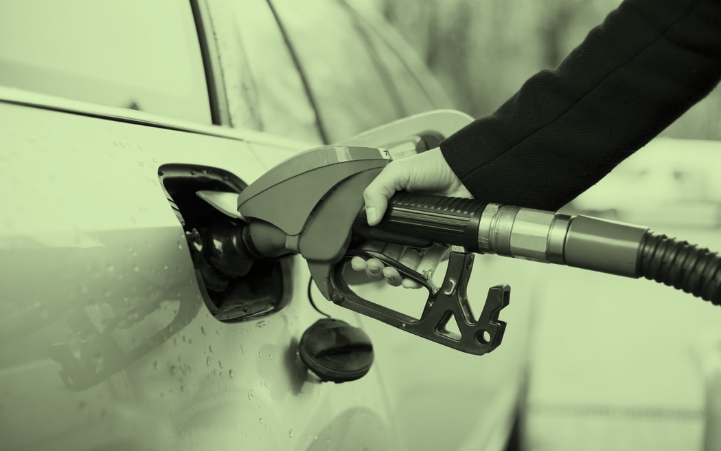 The image shows petrol being pumped into a car. The image has a light green wash over it.