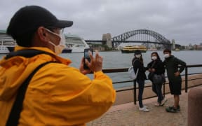 People wear face masks as a preventative measure against Coronavirus COVID-19 in front of the Sydney Harbour Bridge in Sydney, Australia on March 14, 2020.