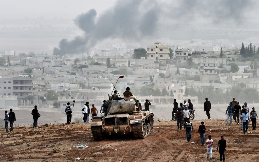 Turkish soldiers on a tank and Kurdish people looking towards Kobane from a hill on the Turkish-Syrian border.
