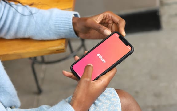 A woman holds a phone with the Tinder app open