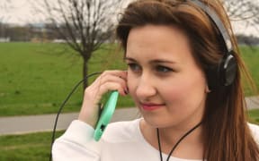 young woman in park wearing headphones with smartphone