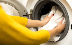 Woman hand loading dirty clothes in washing machine.